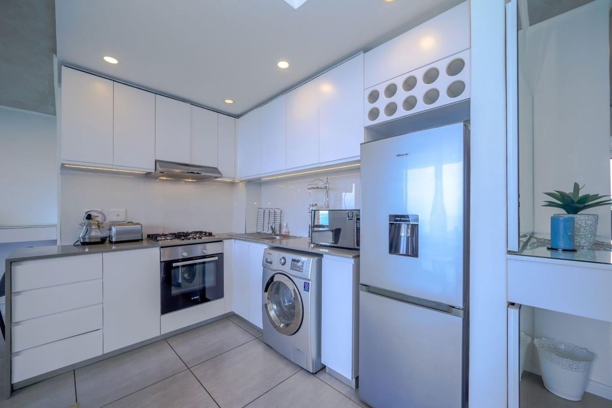 Modern kitchen featuring sleek white cabinetry, integrated gas hob, electric oven, extractor fan, and tiled flooring with ample storage space.