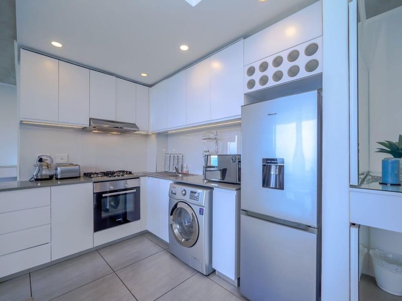 Modern kitchen featuring sleek white cabinetry, integrated gas hob, electric oven, extractor fan, and tiled flooring with ample storage space.