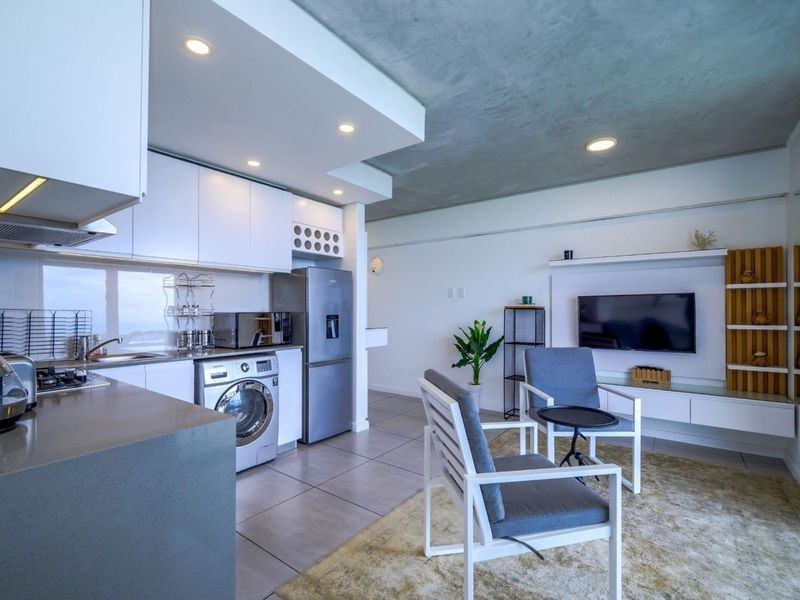 Modern open-plan living area featuring a sleek kitchen with stone countertops, integrated appliances, and a dedicated media wall with built-in shelving.