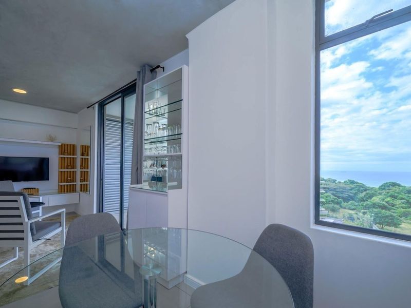 Open plan living area featuring a built-in display cabinet, large windows with scenic coastal views, and access to a balcony through sliding glass doors.