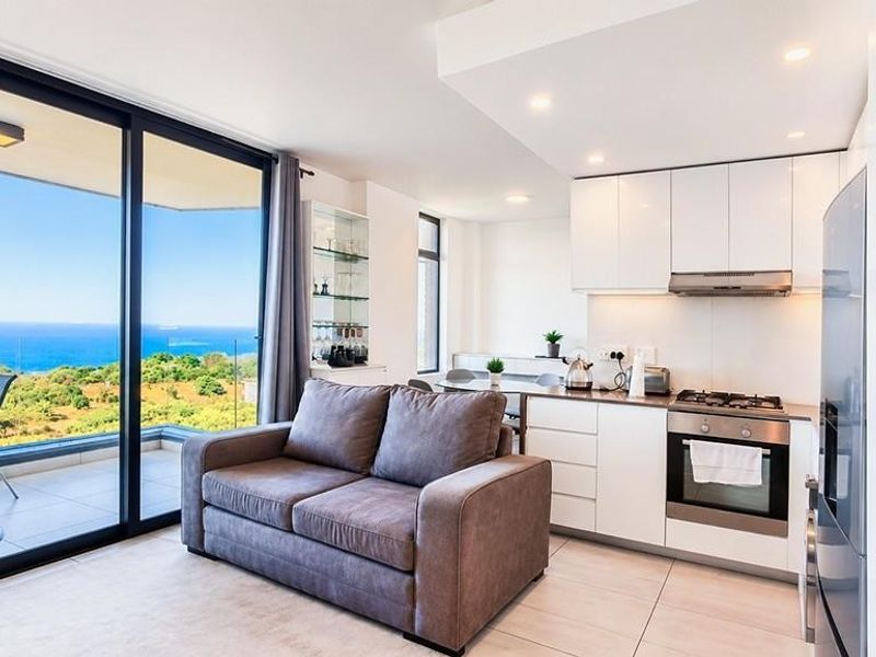 Modern open-plan living area featuring a sleek kitchen with built-in appliances and large sliding doors opening to a balcony with expansive ocean views.