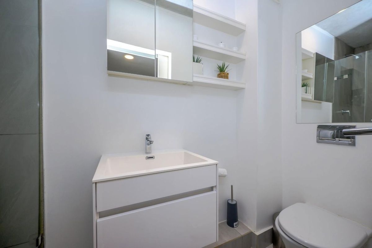 A modern, clean bathroom featuring a white vanity with basin, wall-mounted mirrored cabinet, open shelving, and a wall-hung toilet with a concealed cistern.