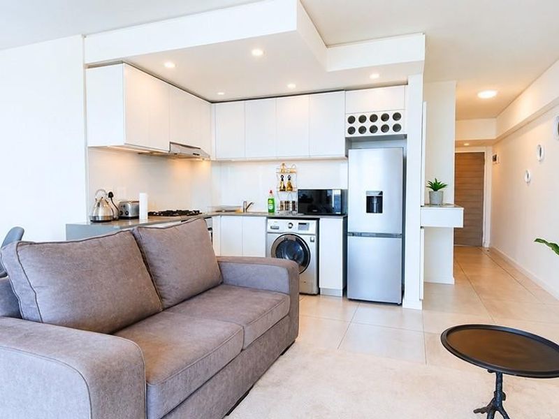 Modern open-plan living area featuring a sleek kitchen with built-in cabinetry, integrated appliances, and neutral tiled flooring throughout the space.
