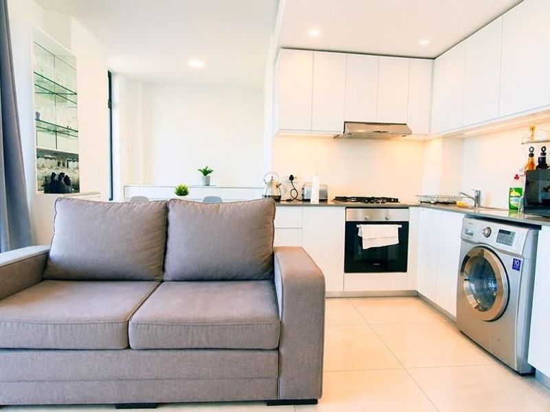Modern open-plan apartment featuring a sleek kitchen with built-in appliances, tiled flooring, and recessed lighting, seamlessly connected to the living area with scenic views.