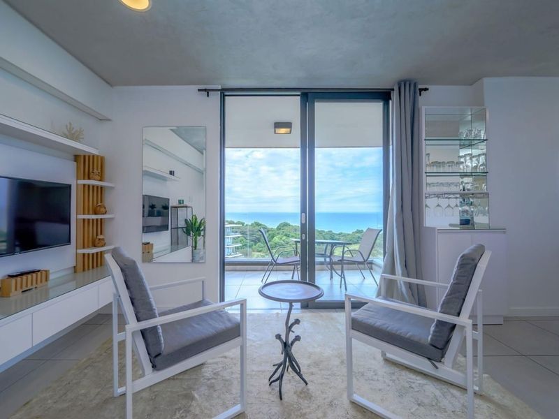Bright living room featuring built-in cabinetry, glass display shelving, and large sliding doors opening to a balcony with scenic ocean views.
