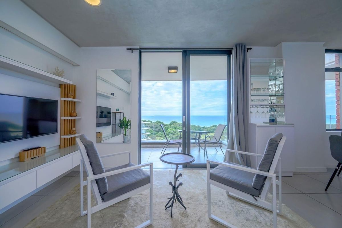 Bright living room featuring built-in cabinetry, glass display shelving, and large sliding doors opening to a balcony with scenic ocean views.