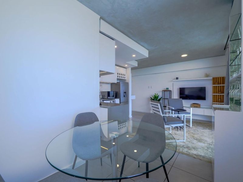 Modern open-plan living area featuring tiled floors, exposed concrete ceilings, recessed lighting, and a compact, well-integrated kitchen space.