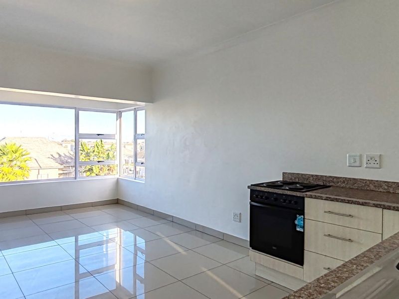 An open-plan living and kitchen area featuring tiled flooring, built-in cabinetry with laminate countertops, and large windows providing ample natural light.