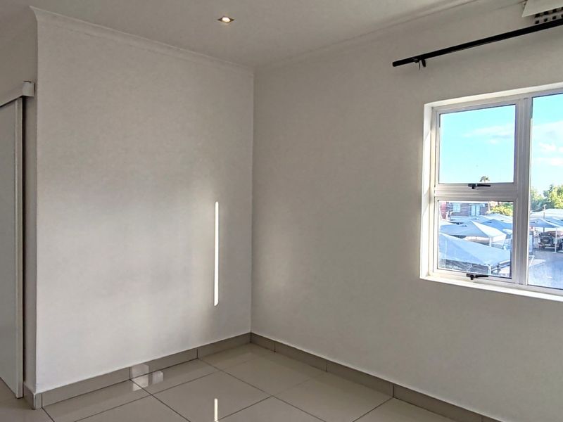 A bright, empty bedroom featuring neutral tiled flooring, recessed downlighting, and a large window with views of the surrounding area.