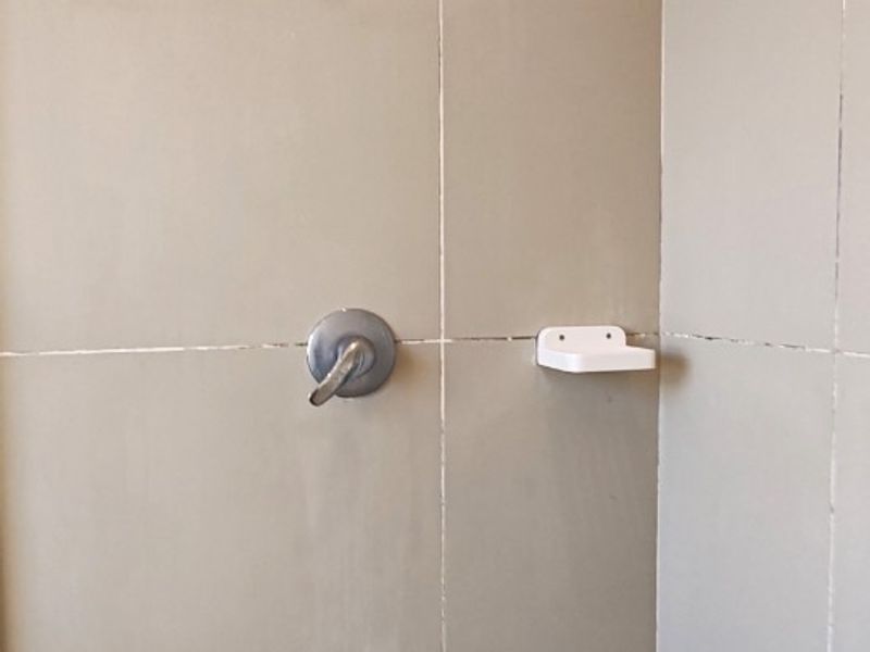 A shower enclosure featuring neutral wall tiles, a standard shower head, mixer tap, and a built-in soap dish.