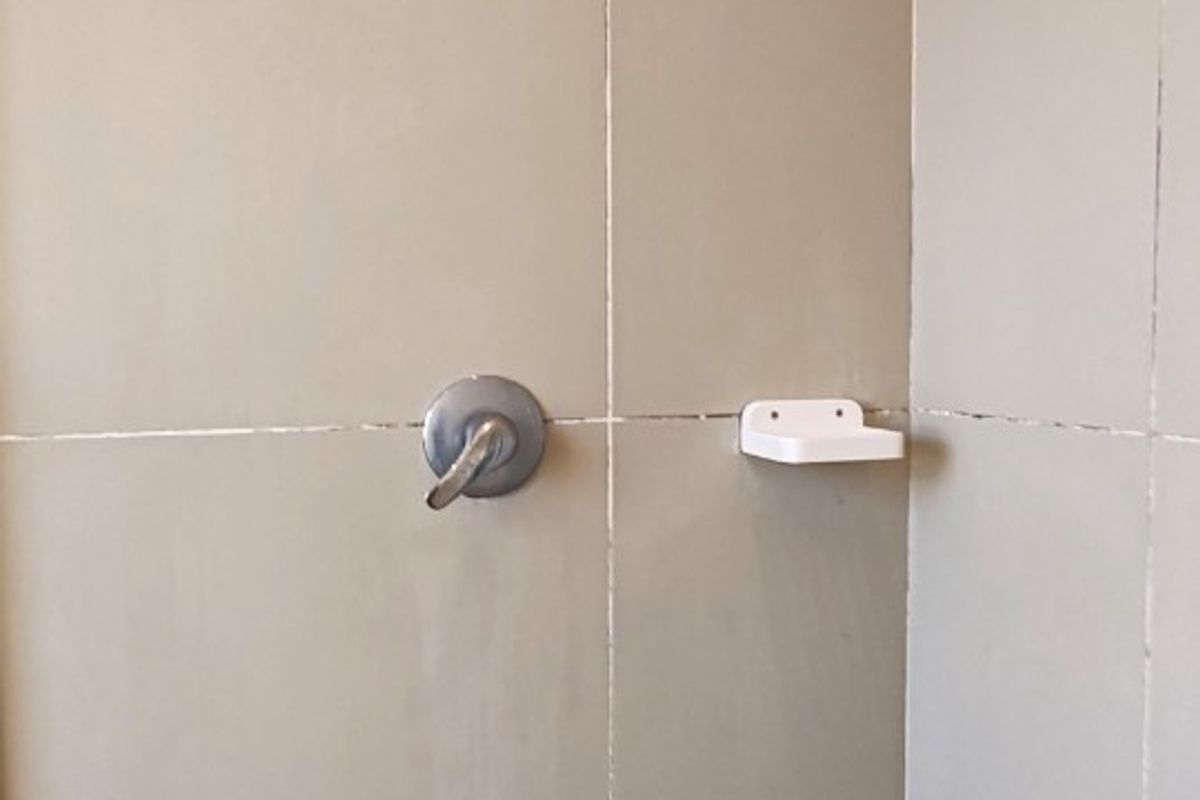 A shower enclosure featuring neutral wall tiles, a standard shower head, mixer tap, and a built-in soap dish.