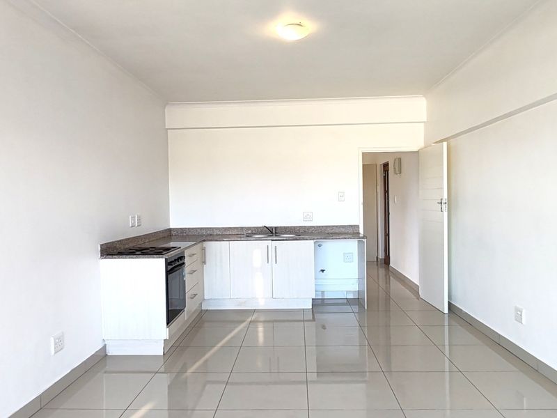 An open-plan living and kitchen area featuring tiled flooring, white walls, and a functional kitchen with built-in cabinetry, granite countertops, and integrated appliances.
