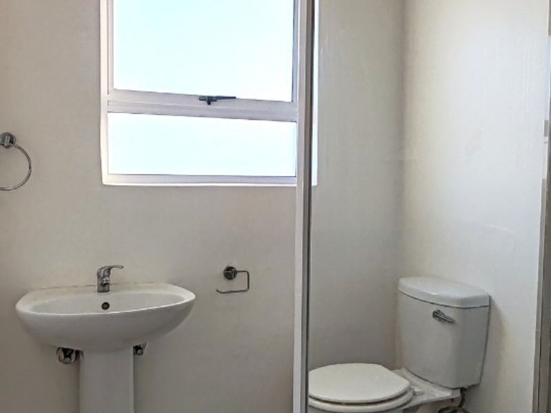 A clean, functional bathroom featuring a pedestal basin, toilet, and a glass-enclosed shower with tiled flooring and an extractor fan.