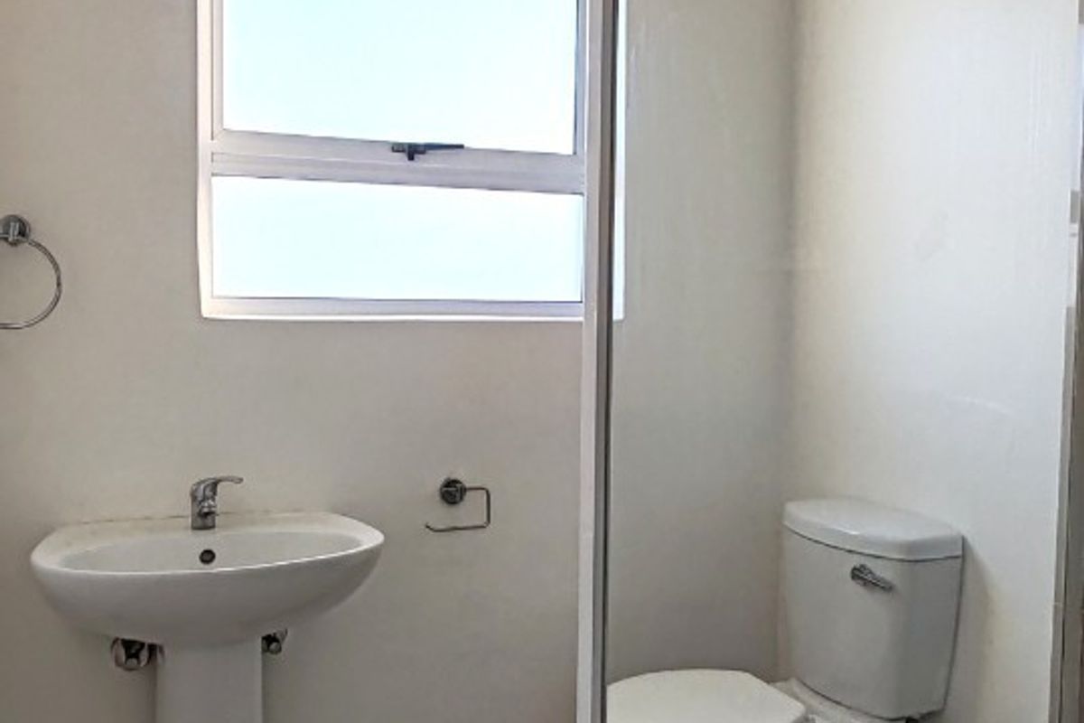 A clean, functional bathroom featuring a pedestal basin, toilet, and a glass-enclosed shower with tiled flooring and an extractor fan.