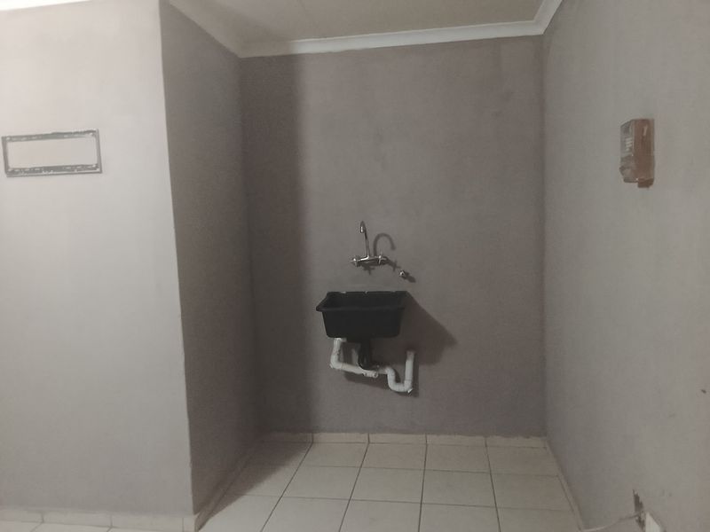 A basic utility or laundry area featuring a wall-mounted sink, exposed plumbing, and tiled flooring, currently in an unfinished state.