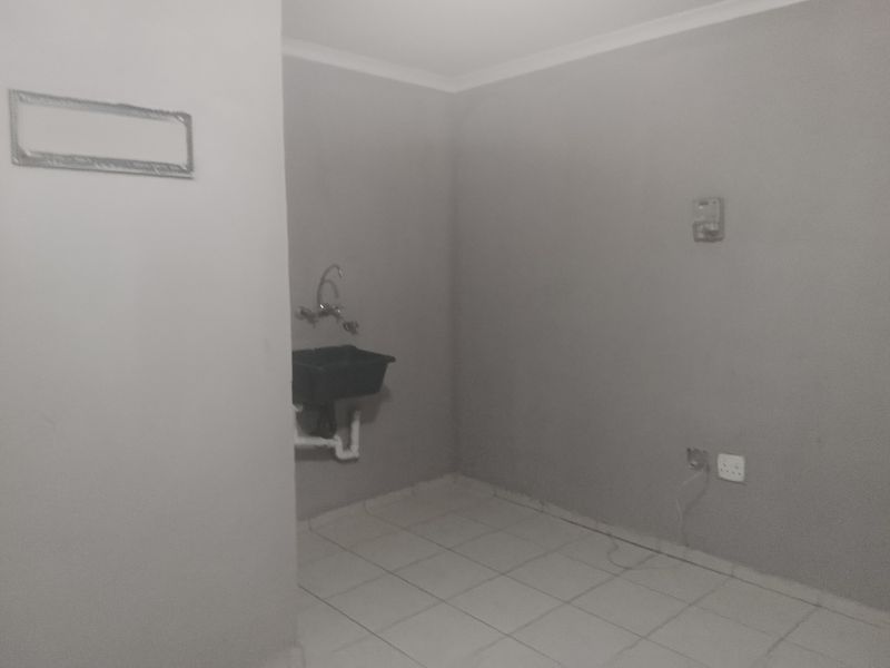 A functional, empty laundry area featuring tiled flooring, a wall-mounted sink, and an installed prepaid electricity meter.
