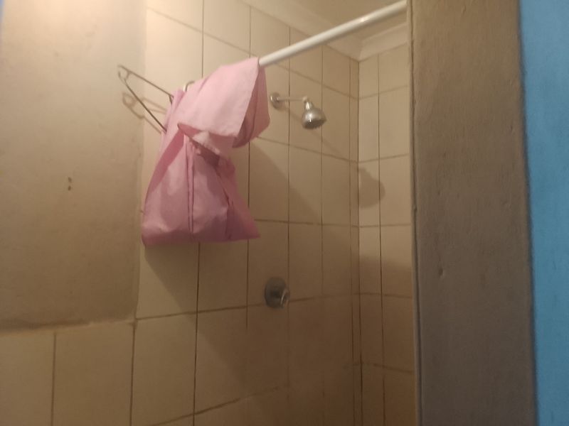 A basic shower enclosure featuring tiled walls, a standard shower head, and mixer tap, currently showing signs of wear.