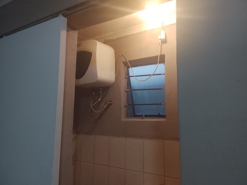 A utility area featuring an electric water heater mounted on a wall with a small louvered window and security bars.
