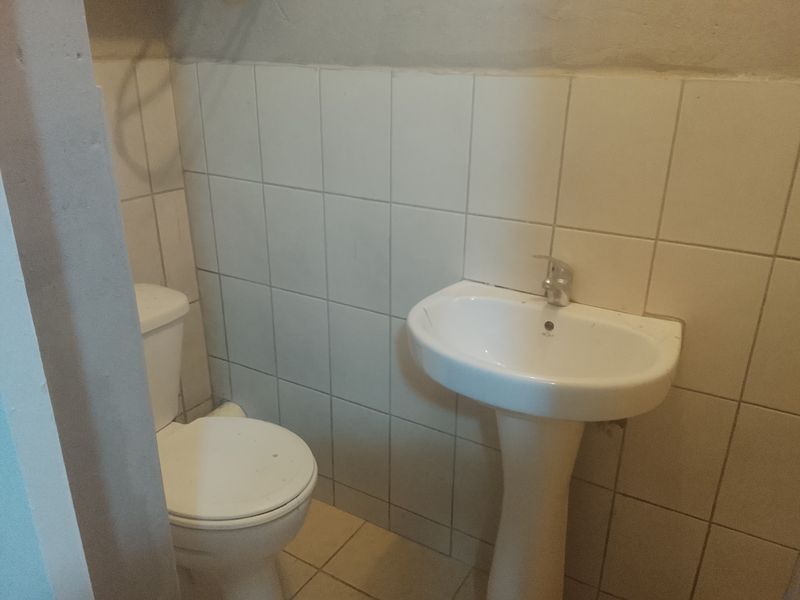 A compact bathroom featuring a pedestal basin and toilet with tiled walls and flooring, requiring cosmetic updates to improve its overall condition.