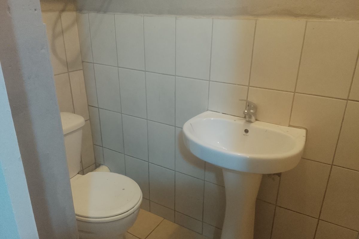 A compact bathroom featuring a pedestal basin and toilet with tiled walls and flooring, requiring cosmetic updates to improve its overall condition.