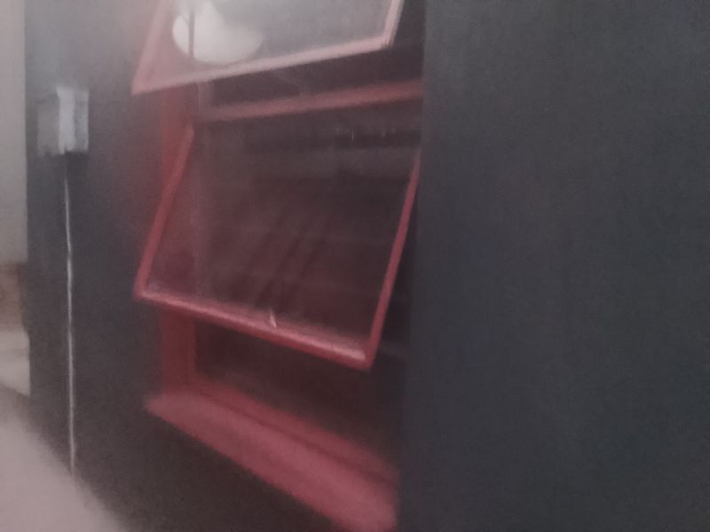A close-up view of a top-hung window with a red frame set against a dark painted exterior wall.