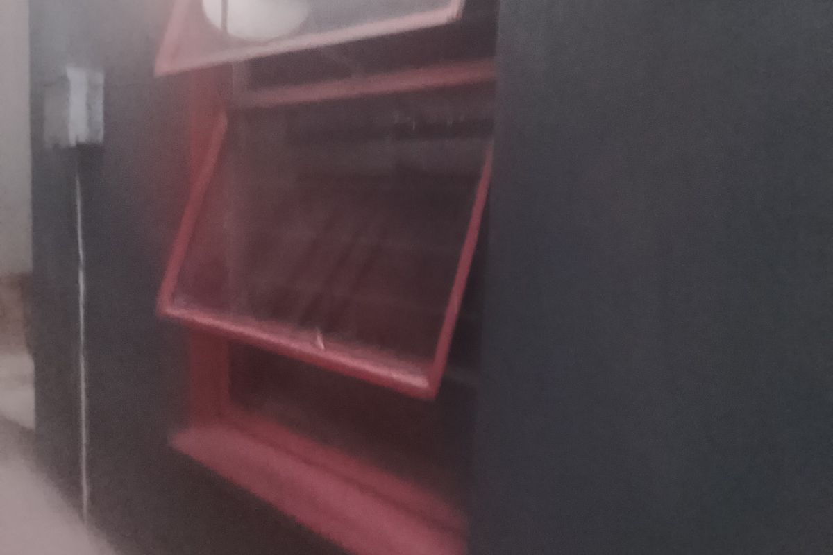 A close-up view of a top-hung window with a red frame set against a dark painted exterior wall.