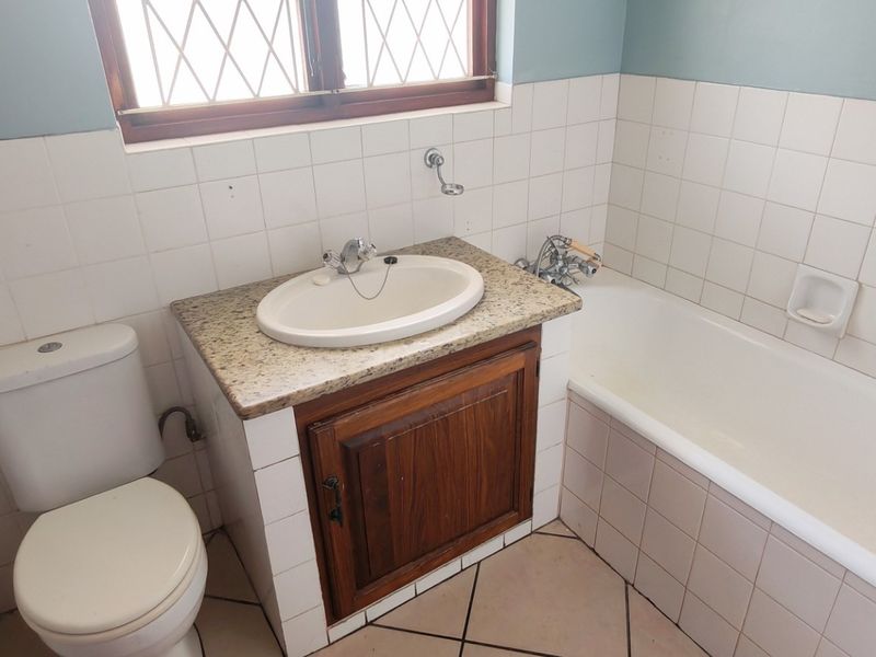 A dated bathroom featuring a vanity with granite countertop, a standard bathtub, and tiled finishes throughout, offering potential for a modern renovation.