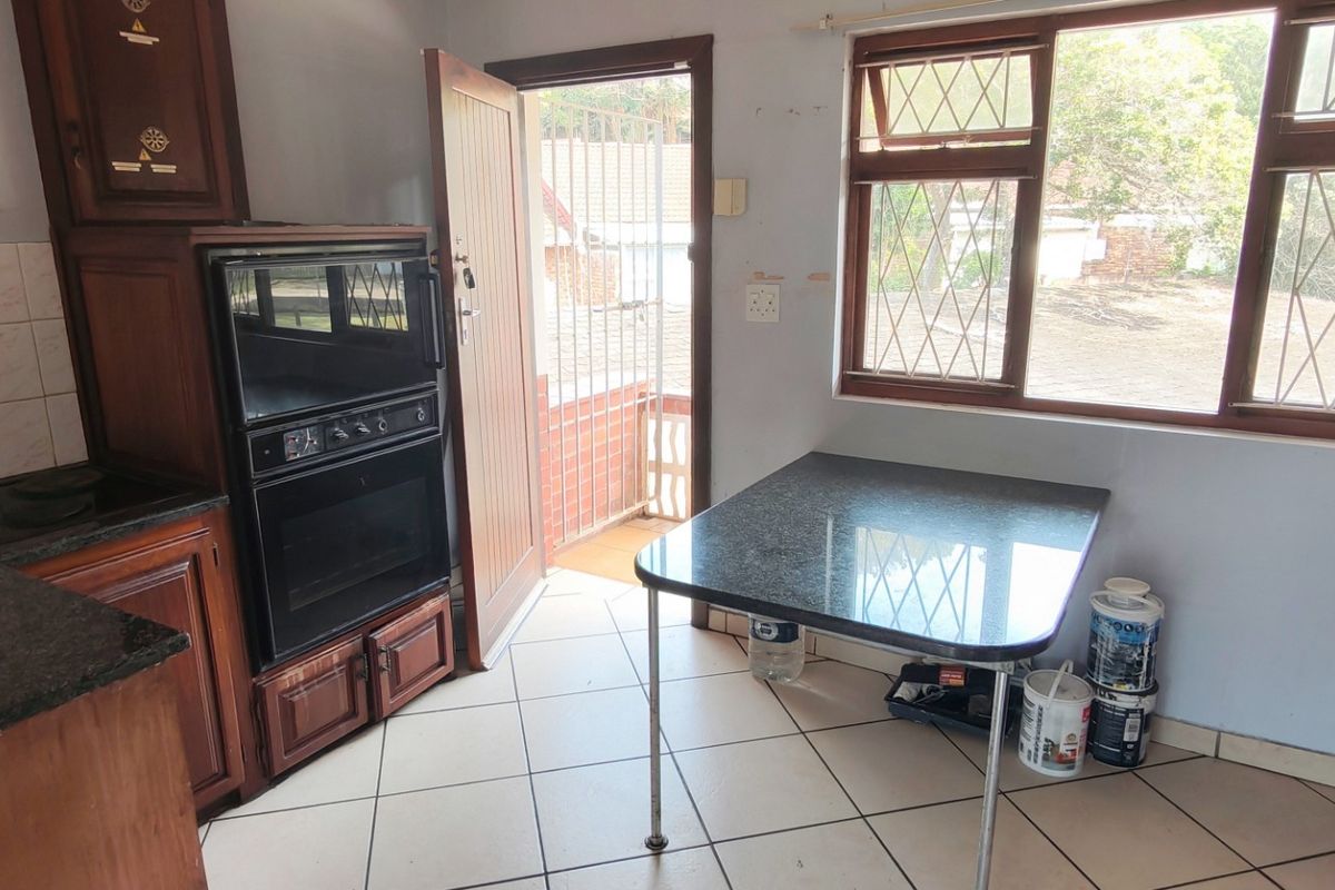A dated kitchen featuring wooden cabinetry, granite countertops, and a built-in double oven, with direct access to an outdoor area.