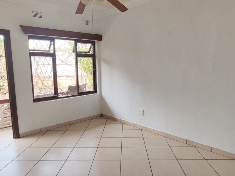 An empty bedroom featuring tiled flooring, a ceiling fan, and direct access to a private balcony through a wooden door.