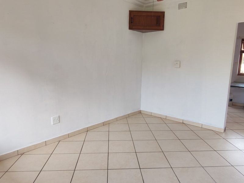 An empty living area featuring ceramic floor tiles, a corner wall cabinet, and neutral white walls, providing a blank canvas for interior design.