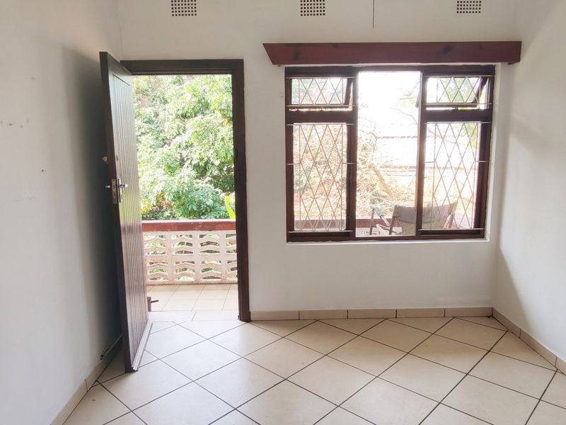An empty bedroom featuring tiled floors, diamond-pattern security bars on the windows, and direct access to an outdoor balcony area.