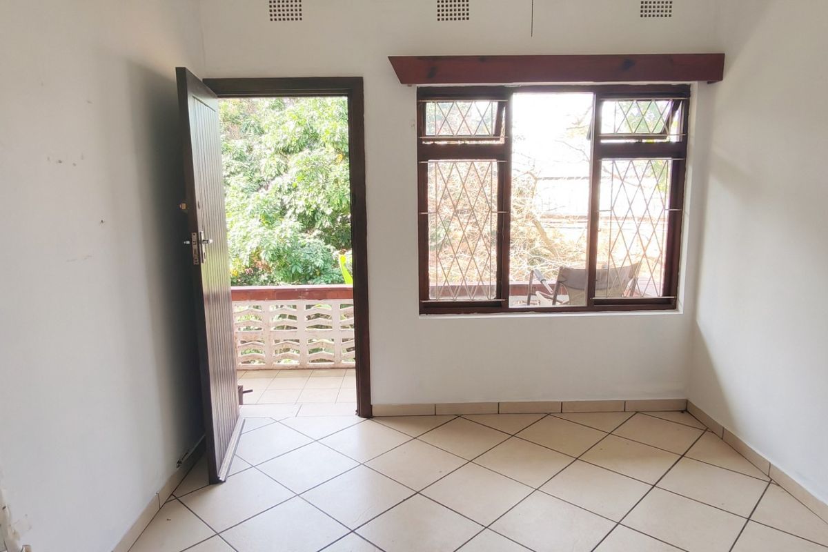 An empty bedroom featuring tiled floors, diamond-pattern security bars on the windows, and direct access to an outdoor balcony area.