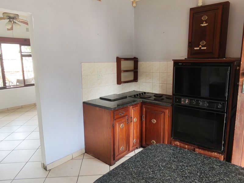 A functional kitchen featuring wooden cabinetry, granite countertops, and a built-in oven, with an adjacent view into a tiled living area.