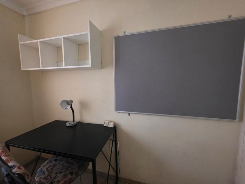 A functional home office space featuring wall-mounted shelving and a large notice board, providing a dedicated area for work or study.
