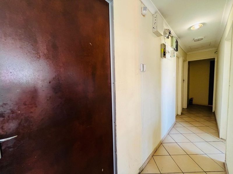 A functional hallway featuring tiled flooring, recessed lighting, and wall-mounted electrical and security infrastructure.