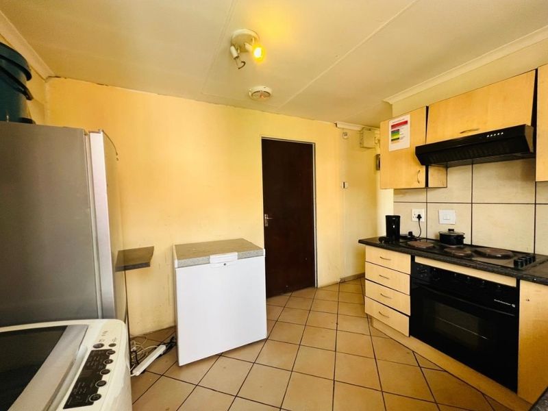 A functional kitchen featuring built-in cabinetry, an electric hob, oven, extractor fan, and tiled flooring, offering potential for cosmetic updates.