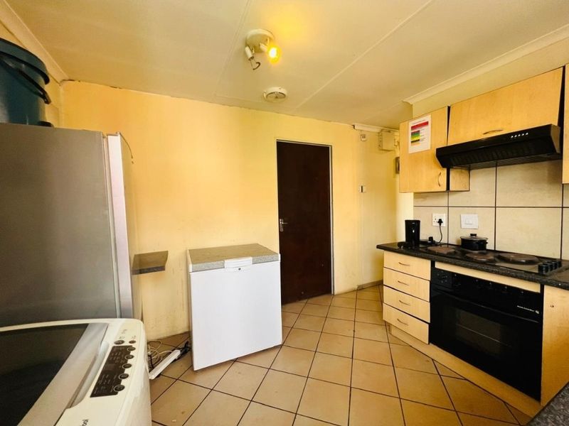 A functional kitchen featuring built-in cabinetry, an electric hob, oven, extractor fan, and tiled flooring, requiring cosmetic updates to improve its overall aesthetic appeal.