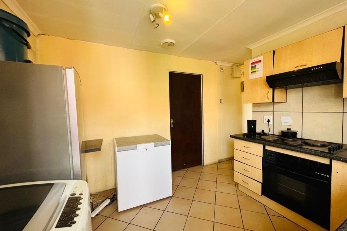 A functional kitchen featuring built-in cabinetry, an electric hob, oven, extractor fan, and tiled flooring, requiring cosmetic updates to improve its overall aesthetic appeal.