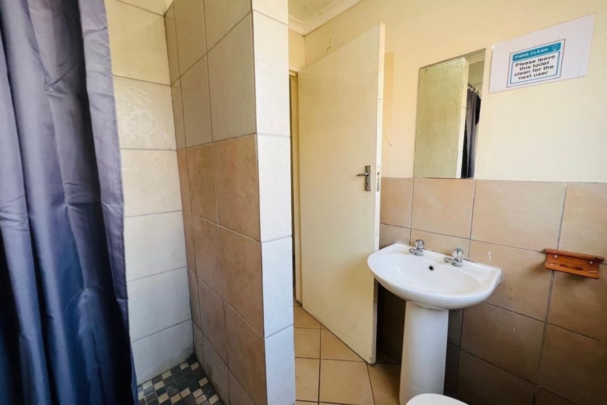 A functional bathroom featuring a pedestal basin, tiled shower enclosure, and neutral wall tiles, offering a blank canvas for potential cosmetic updates.