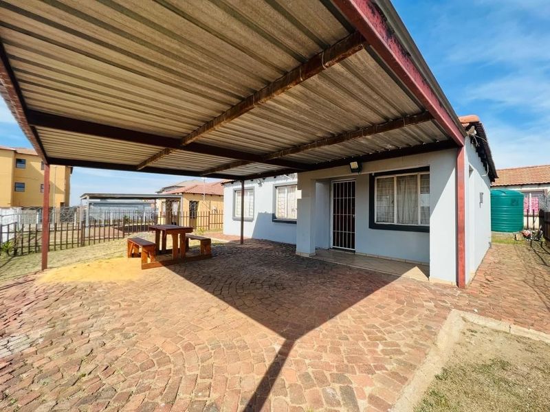 A covered outdoor patio area featuring a corrugated metal roof, steel support structure, and brick paving, providing a functional space for outdoor living.