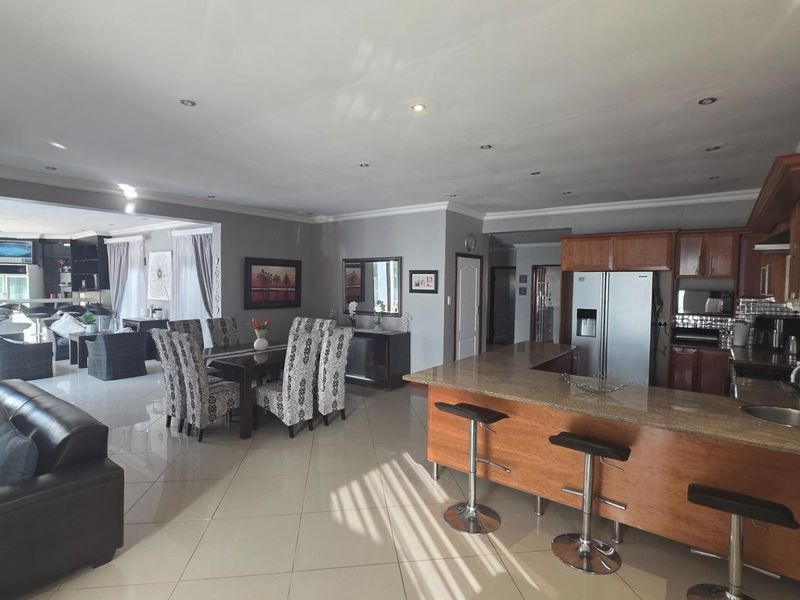 Spacious open-plan living area featuring a kitchen with granite countertops, wooden cabinetry, and a breakfast bar, seamlessly flowing into the dining and lounge spaces.