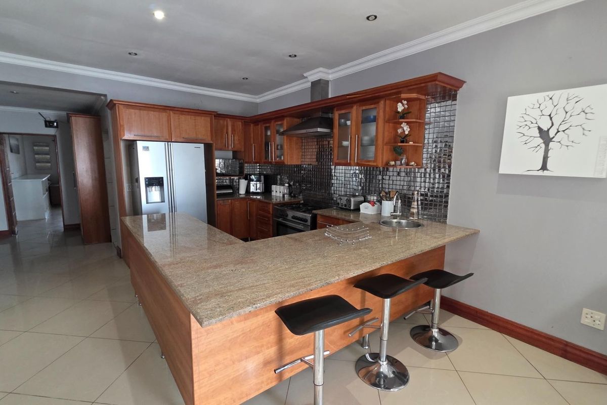 A functional kitchen featuring wooden cabinetry, granite countertops, a mosaic backsplash, and integrated appliances, with an open-plan layout and tiled flooring.