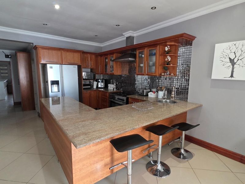 A functional kitchen featuring wooden cabinetry, granite countertops, a mosaic backsplash, and integrated appliances, with an open-plan layout and tiled flooring.