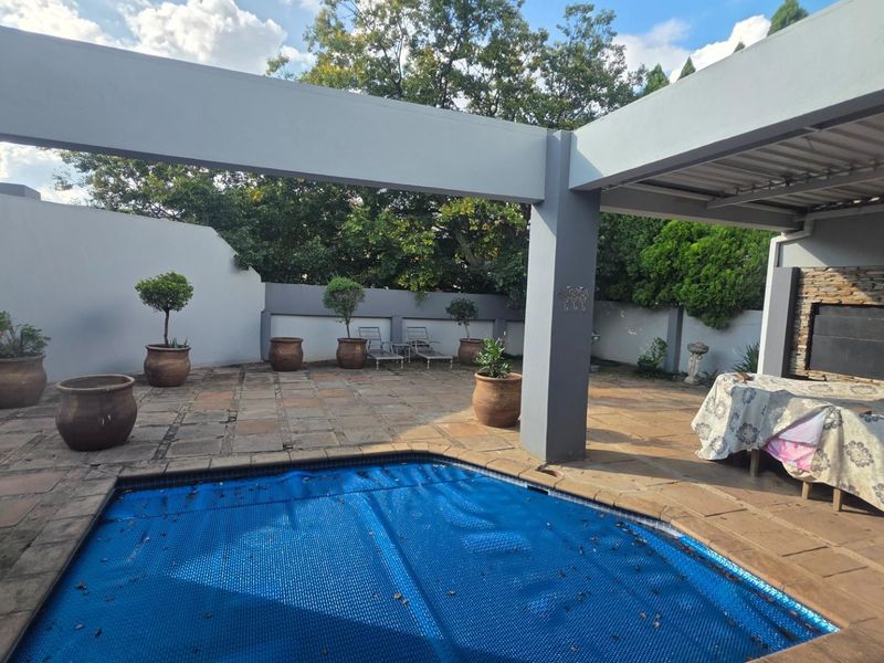 Outdoor pool area featuring a covered patio with stone cladding, paved flooring, and a swimming pool with a protective cover.