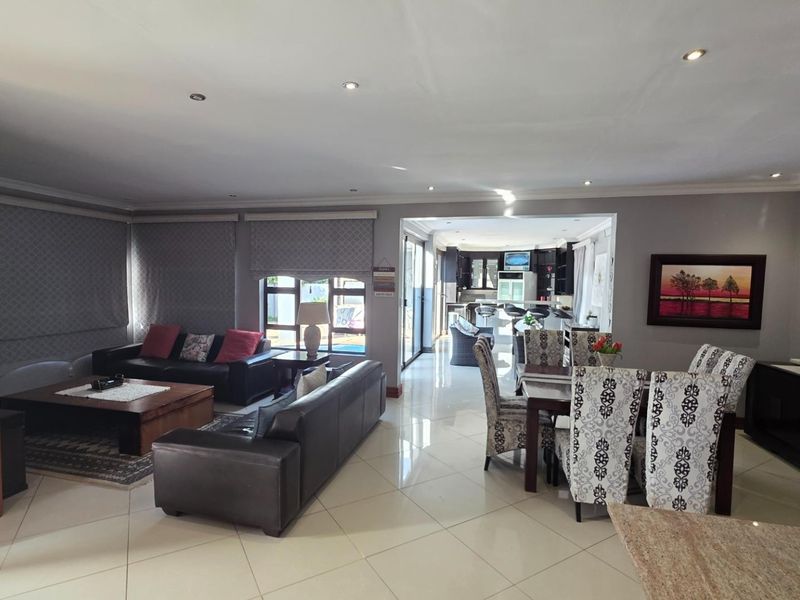 Spacious open-plan living and dining area featuring polished tiled flooring, recessed downlighting, and seamless flow to the kitchen and outdoor patio area.