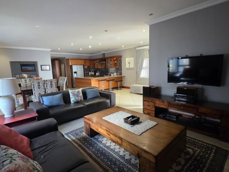 Spacious open-plan living area featuring a modern kitchen with wooden cabinetry, a central island, and tiled flooring, seamlessly flowing into the lounge space.