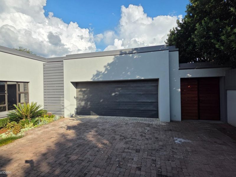 Modern front facade featuring a double garage, paved driveway, and timber entrance door, set against a clean, contemporary architectural design.