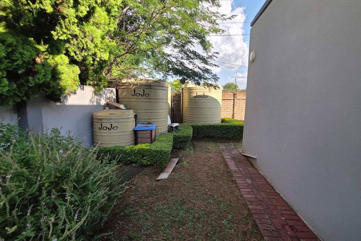 Rear exterior area featuring multiple water storage tanks, brick paving, and established boundary wall with landscaped hedging.