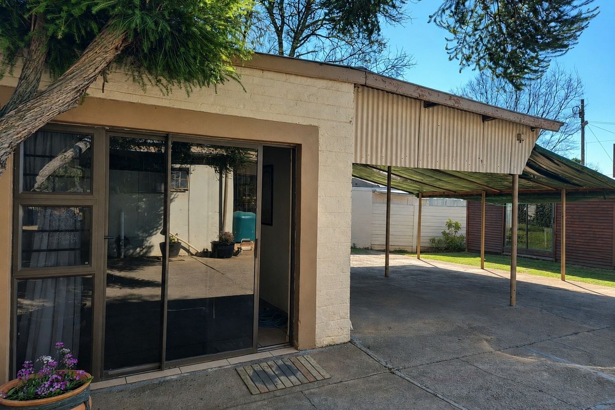 Rear exterior view featuring a covered carport area with corrugated metal roofing and a sliding glass door entrance to the main dwelling.
