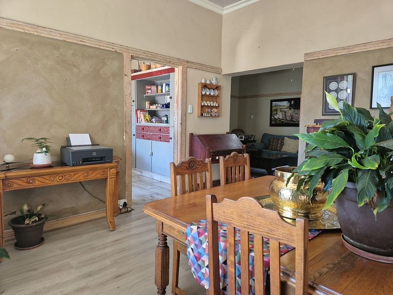 Open plan dining and living area featuring laminate flooring and unfinished wall plastering, with a view into an adjacent scullery or pantry space.